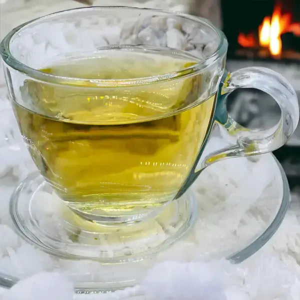 A freshly brewed cup of Night Owl Tea served in a glass cup, with a calming golden hue. The tea is surrounded by soft, frosty snow, evoking a sense of warmth and relaxation perfect for promoting a peaceful night’s sleep.