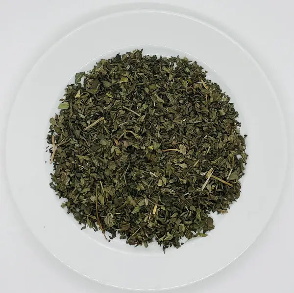 naturally green loose leaves of dried peppermint tea blend on a ceramic plate.